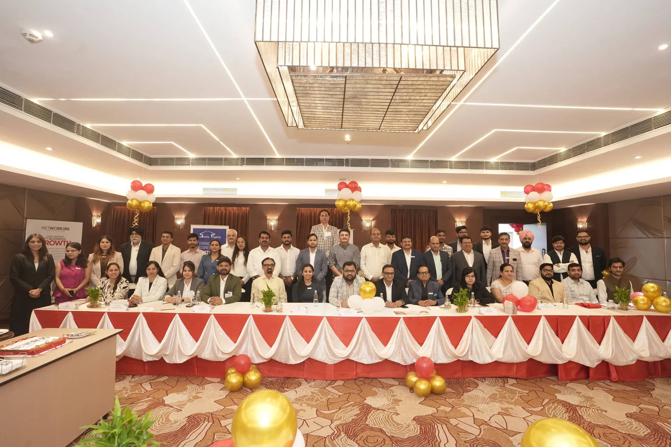 Networkers members seated around a long red-draped table at Hotel Sayaji